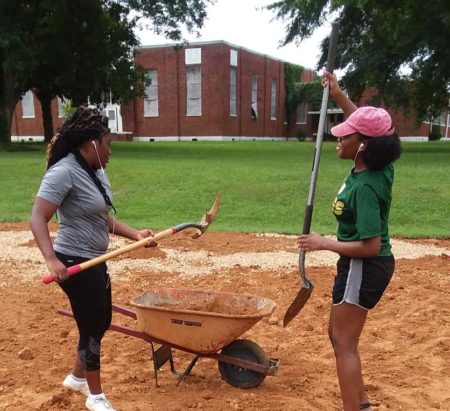 Two community volunteers from Duck Hill, MS, shovel dirth into a wheelbarrow.