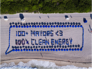 Aerial image of people standing in a pattern to create the message "100 Mayors love 100% Clean Energy"