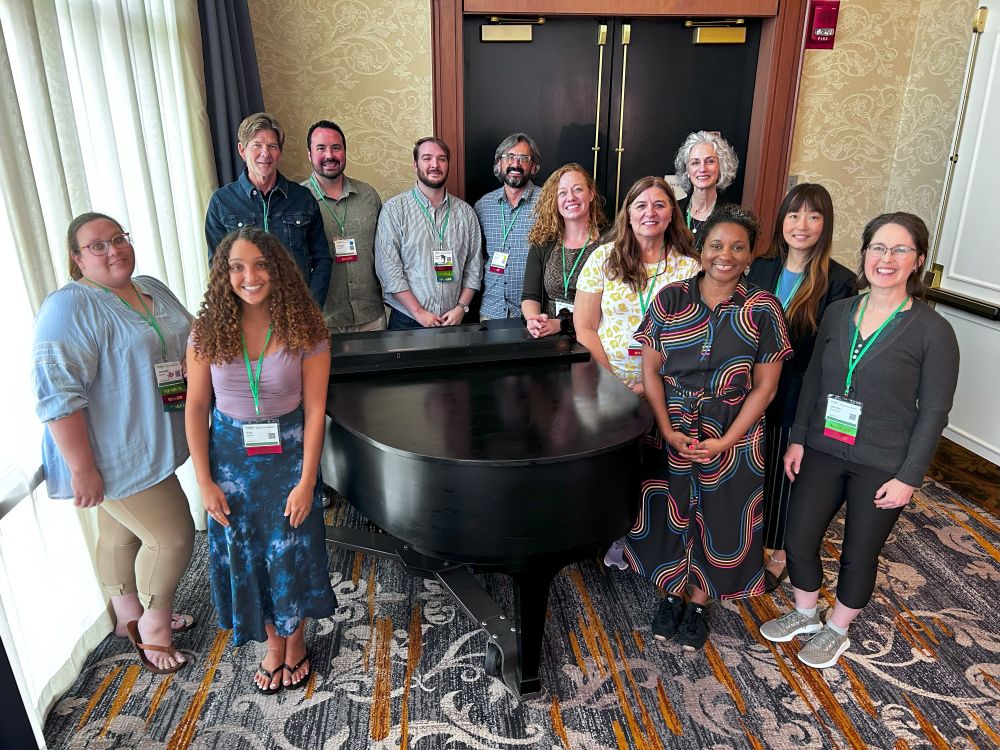 board members in hall way around a piano pose for a picture